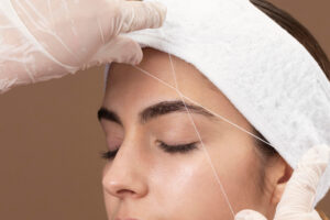 Profissional realizando epilação com linha em sua cliente.